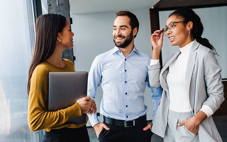 Three individuals, two women and one male, in a professional setting, engaged in a conversation.