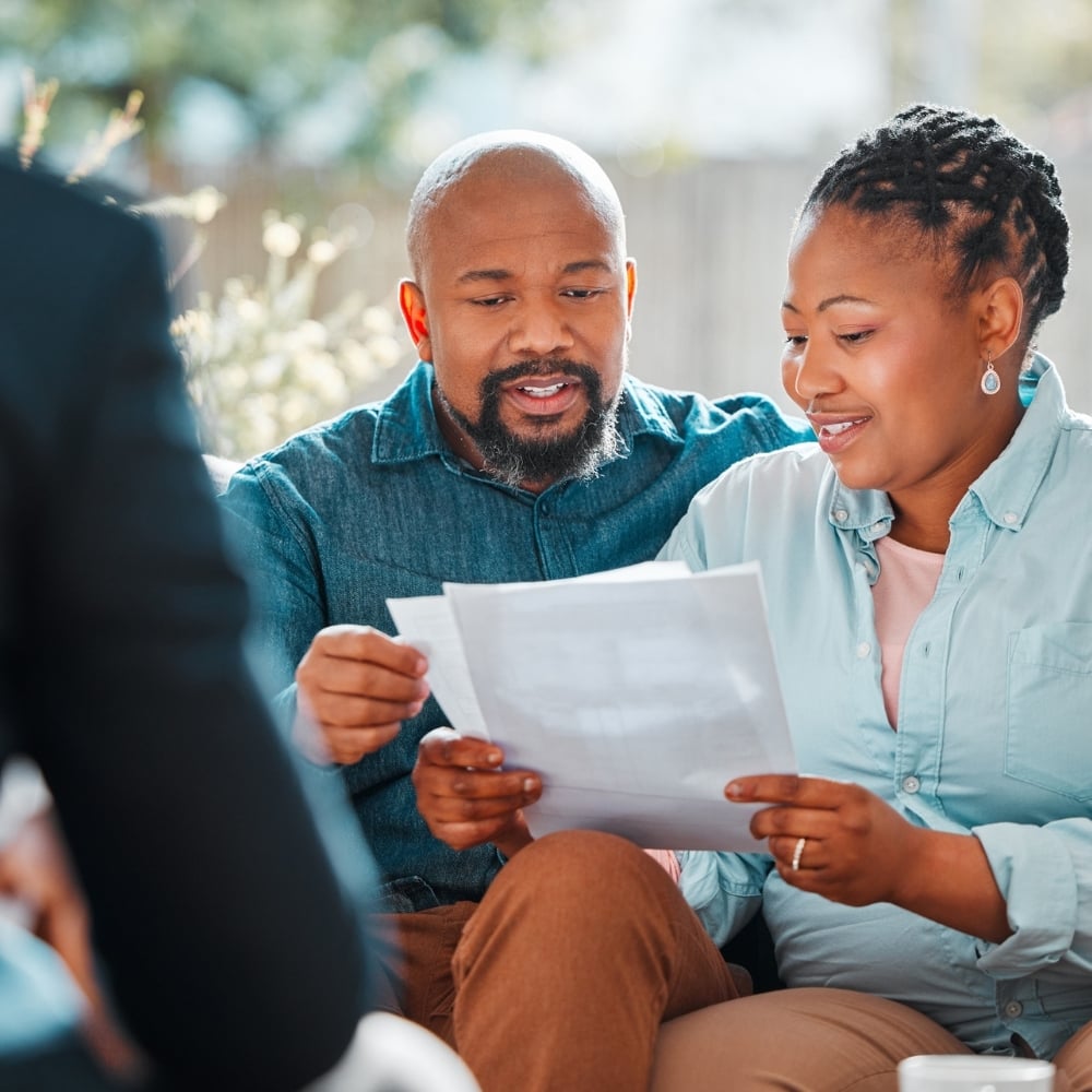 Three individuals sitting closely together, with two of them looking at a document.