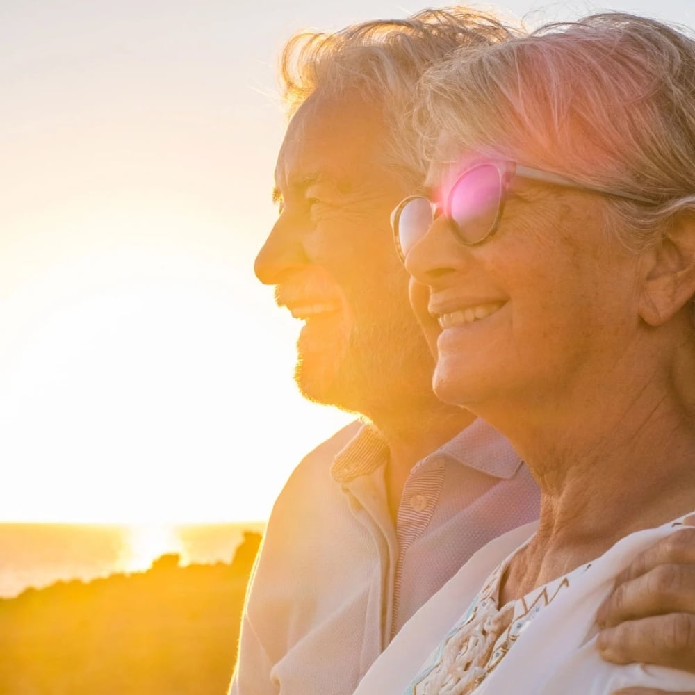 A senior couple smiling while staring at a sunset.